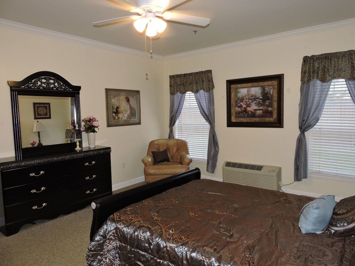 A cozy bedroom featuring a bed, dresser with mirror, armchair, and wall artwork.