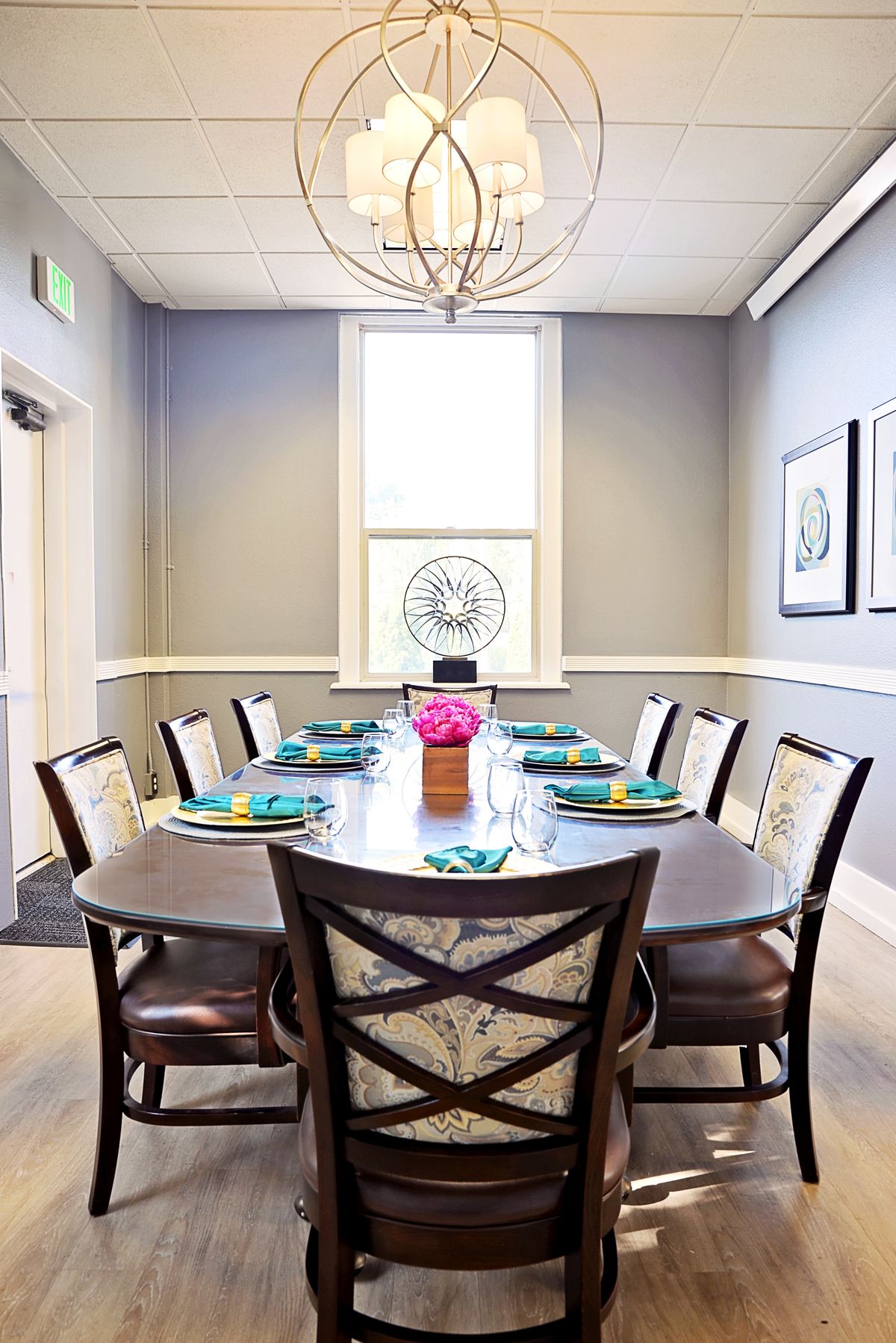 A modern dining room with a large table, surrounded by chairs and adorned with a flower centerpiece.