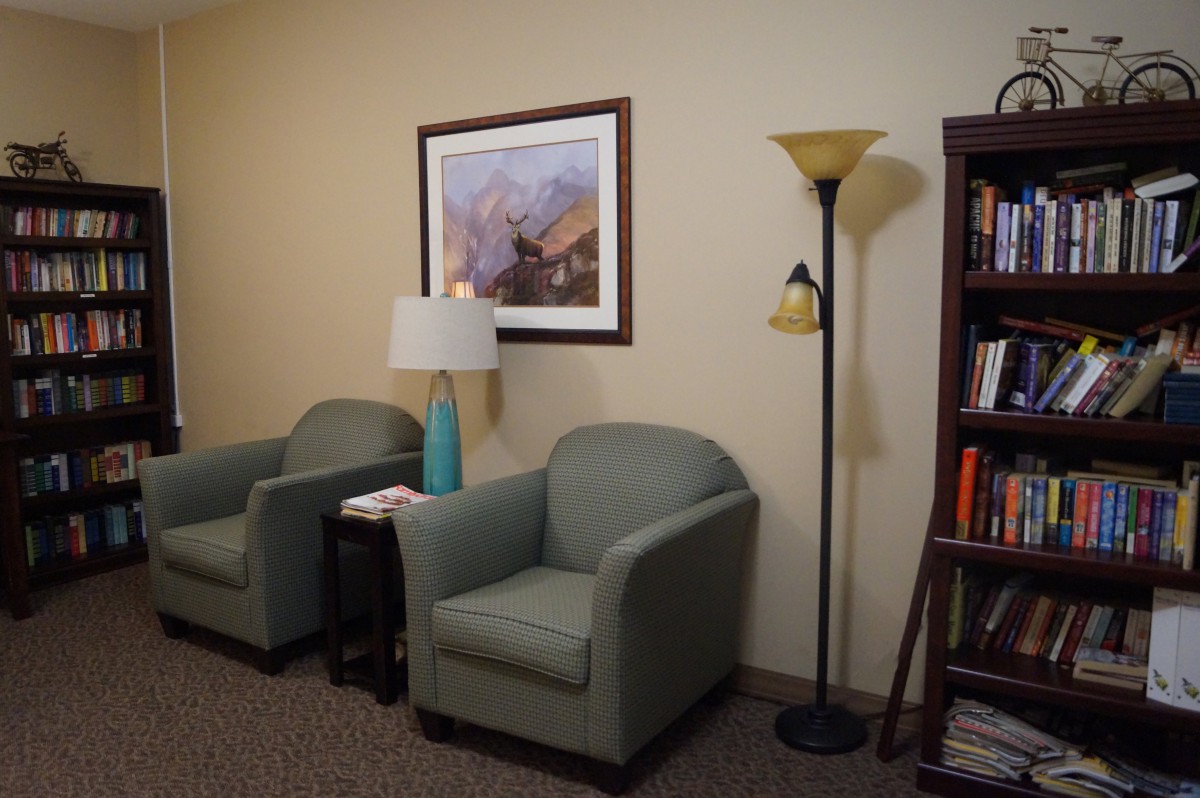 A cozy waiting room with two armchairs, a floor lamp, and a bookshelf.