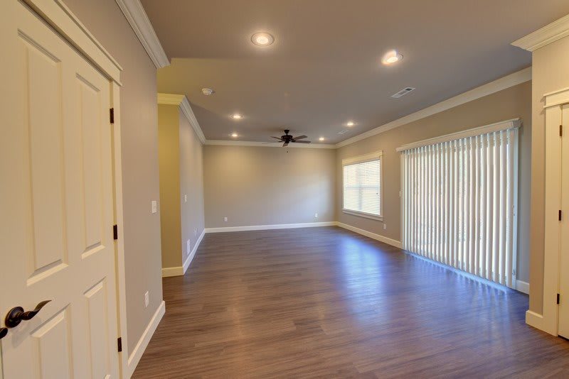 A spacious empty room with hardwood floors, recessed lighting, and a ceiling fan.