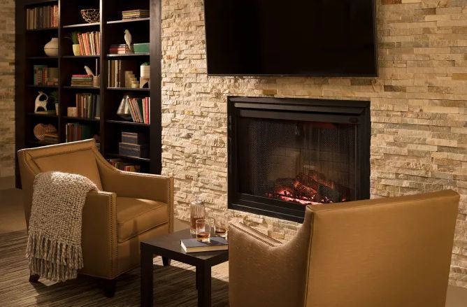 A cozy living room with armchairs by a fireplace and a bookshelf nearby.