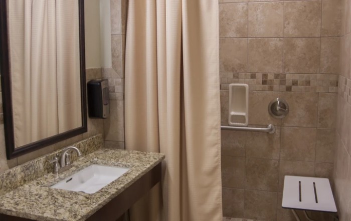 A bathroom with a granite countertop, sink, mirror, and shower curtain.