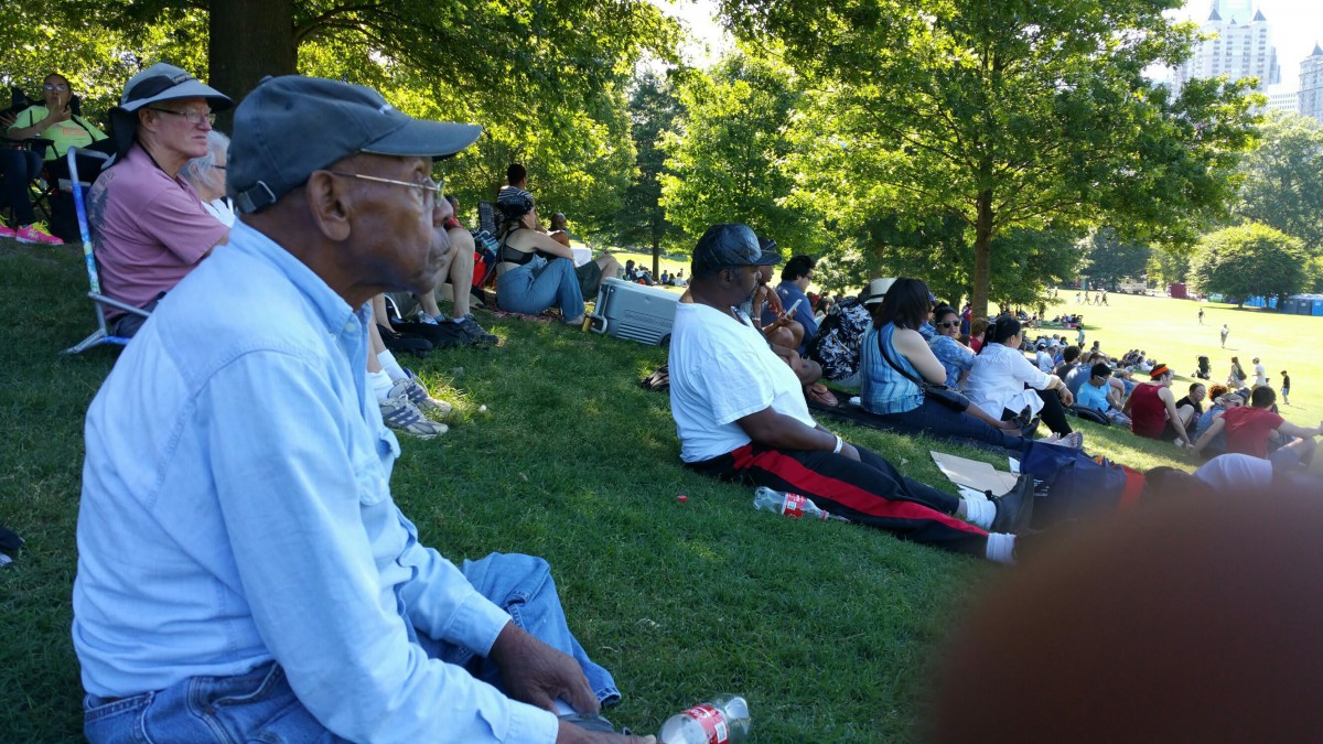 A group of people enjoying a sunny day at the park, sitting on the grass under the shade of trees.