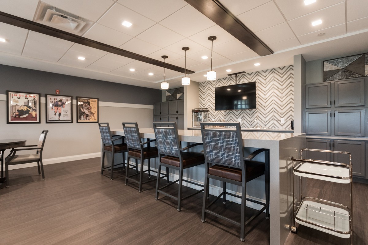 A modern indoor bar featuring sleek counter stools, pendant lighting, and a herringbone patterned backsplash.