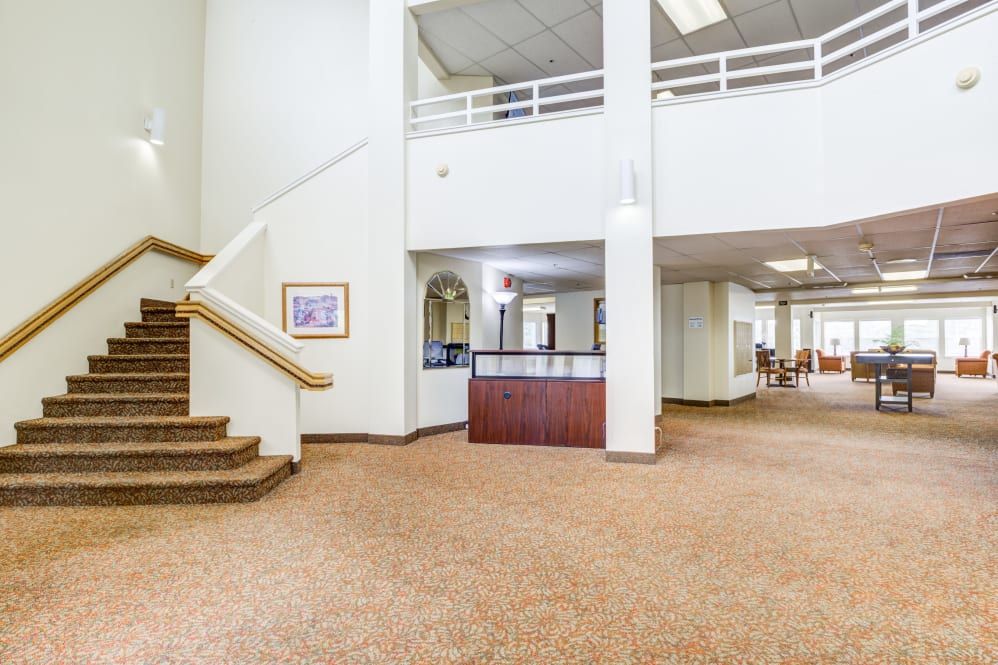 A spacious lobby area with a reception desk, carpeted floors, and a staircase leading to an upper level.