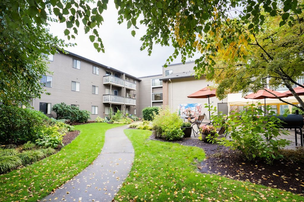 A well-maintained apartment complex with a lush green courtyard and outdoor seating.