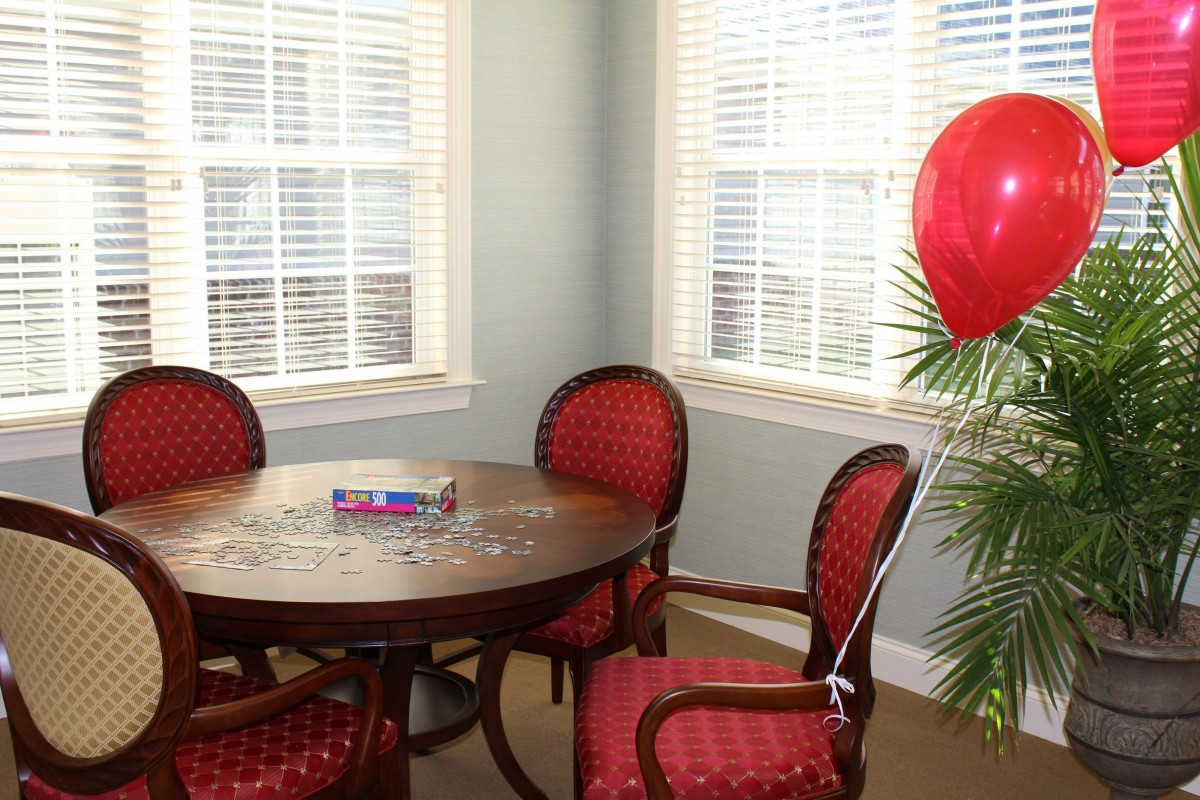 A cozy dining area with a round table, red cushioned chairs, and a red balloon tied to a plant by the window.