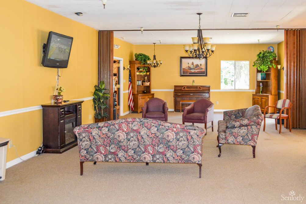 A cozy living room with floral-patterned sofas, a television, and a chandelier.