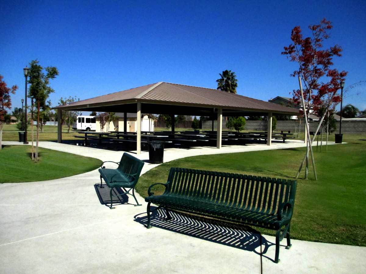 A sunny day at a park with a pavilion and benches along the walkway.