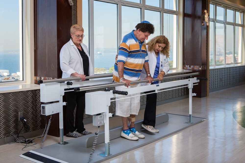 A patient undergoing physical therapy with the assistance of two therapists in a medical facility.