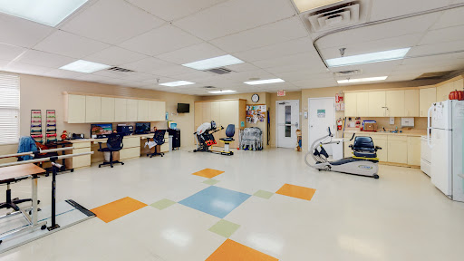A spacious rehabilitation room equipped with various exercise machines and workstations for therapy activities.