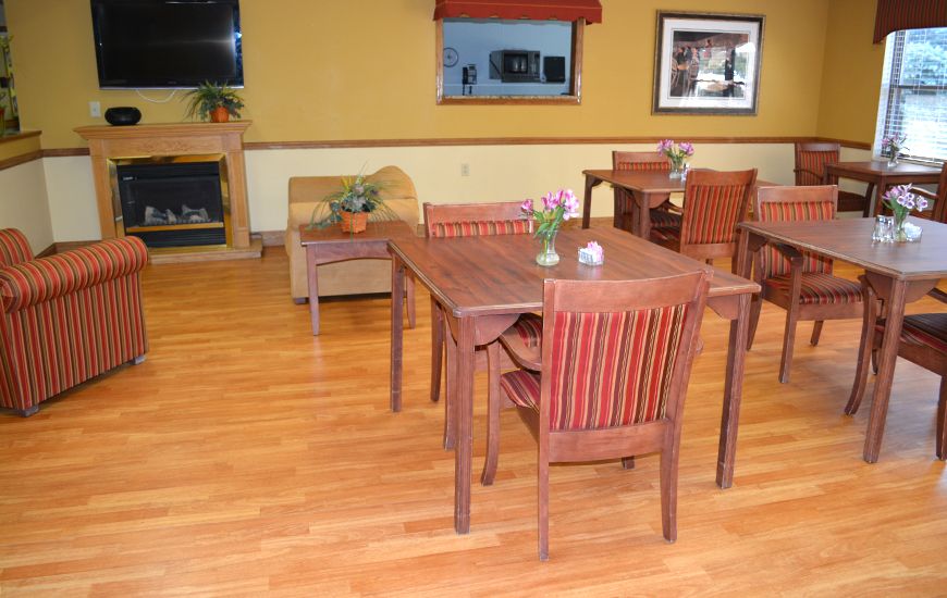 A cozy dining area with wooden tables and chairs, featuring a warm decor and indoor plants.