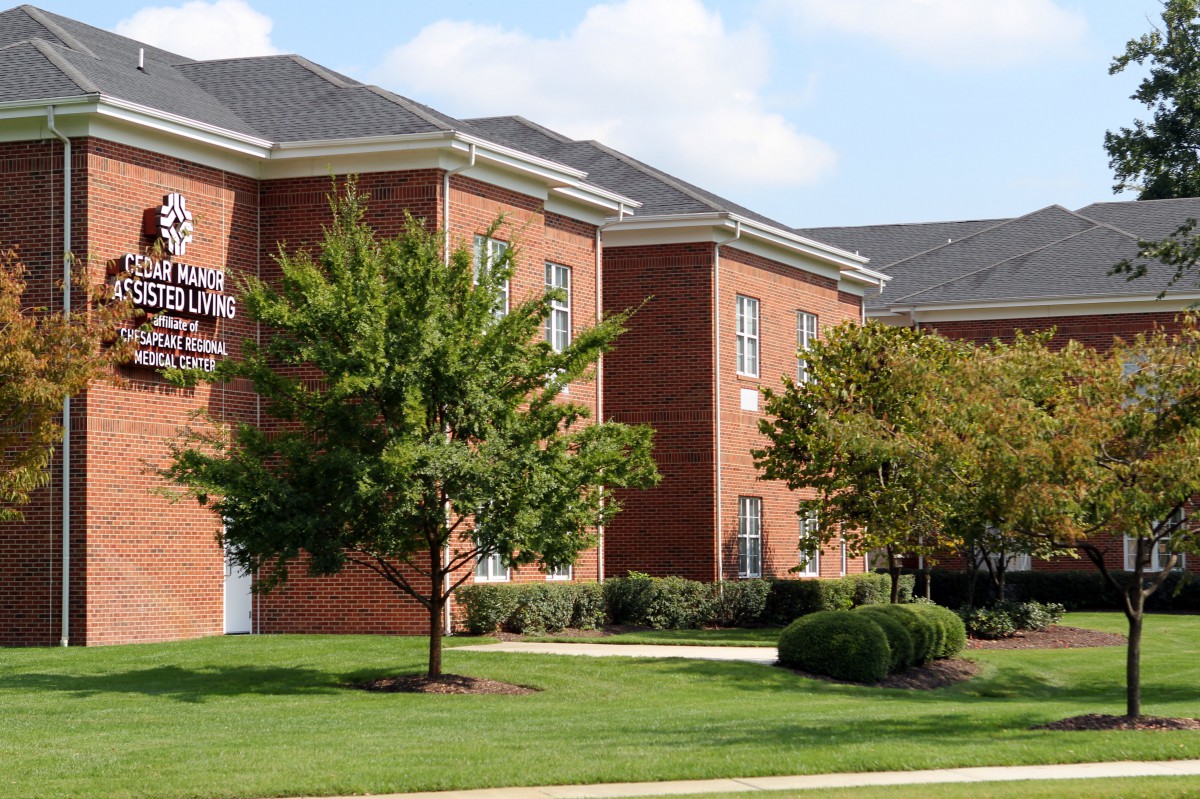 A view of a suburban brick residential building surrounded by trees and a well-maintained lawn.