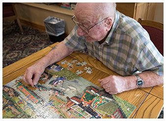 An elderly person working on a jigsaw puzzle at a table.