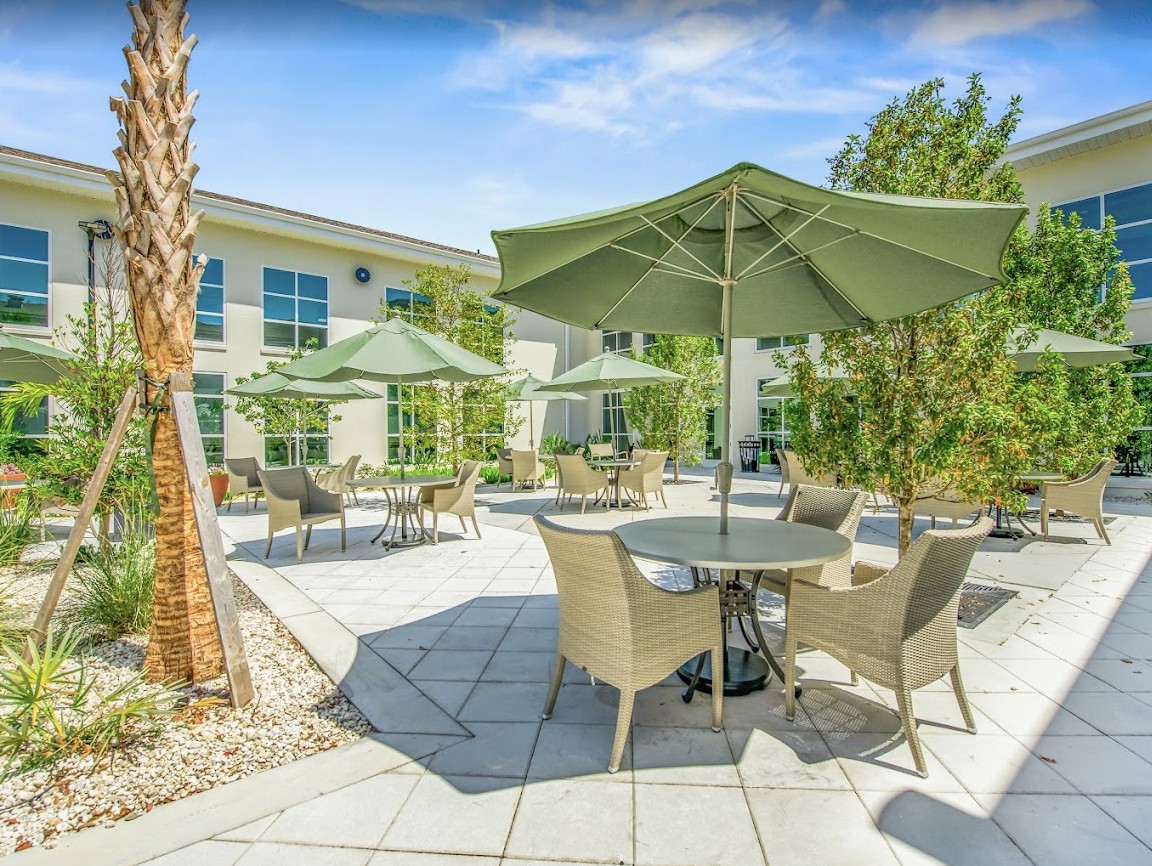 A sunny outdoor patio area with tables, chairs, and large umbrellas.