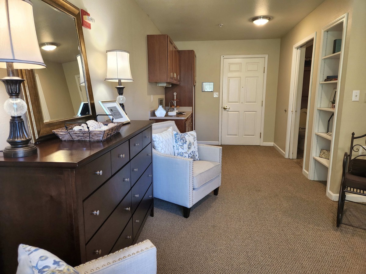 A cozy living room area featuring an armchair, dresser with a mirror, and soft lighting.