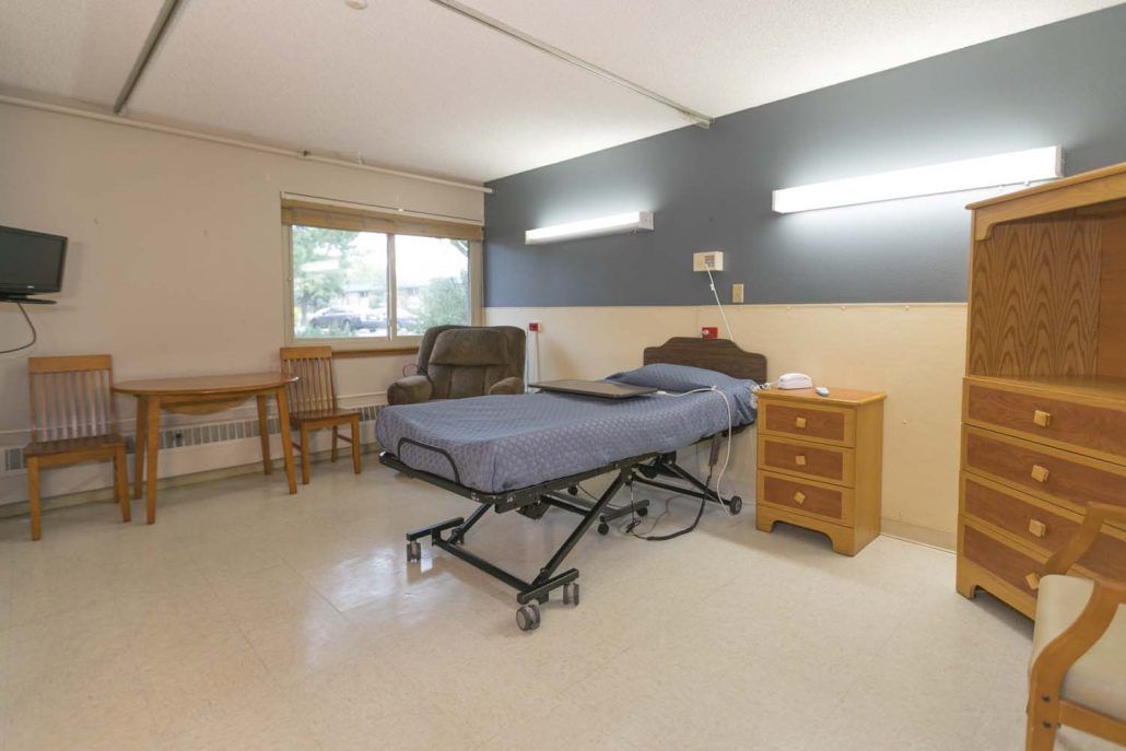 A hospital room with a bed, side table, and chair near a window.