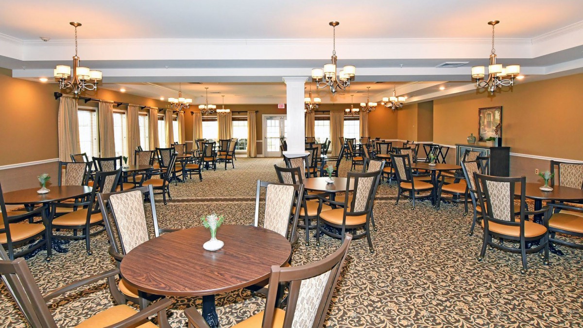 An empty dining area with multiple tables and chairs, a carpeted floor, and chandeliers hanging from the ceiling.