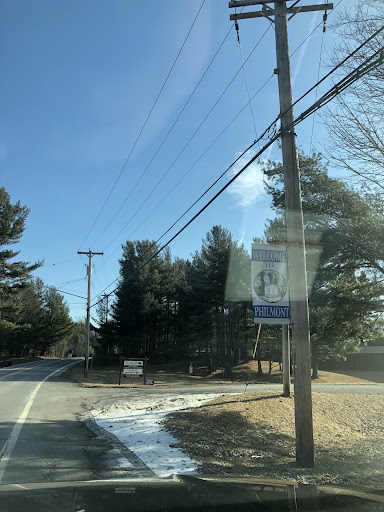 A scenic view of a road lined with trees and power lines under a clear blue sky.