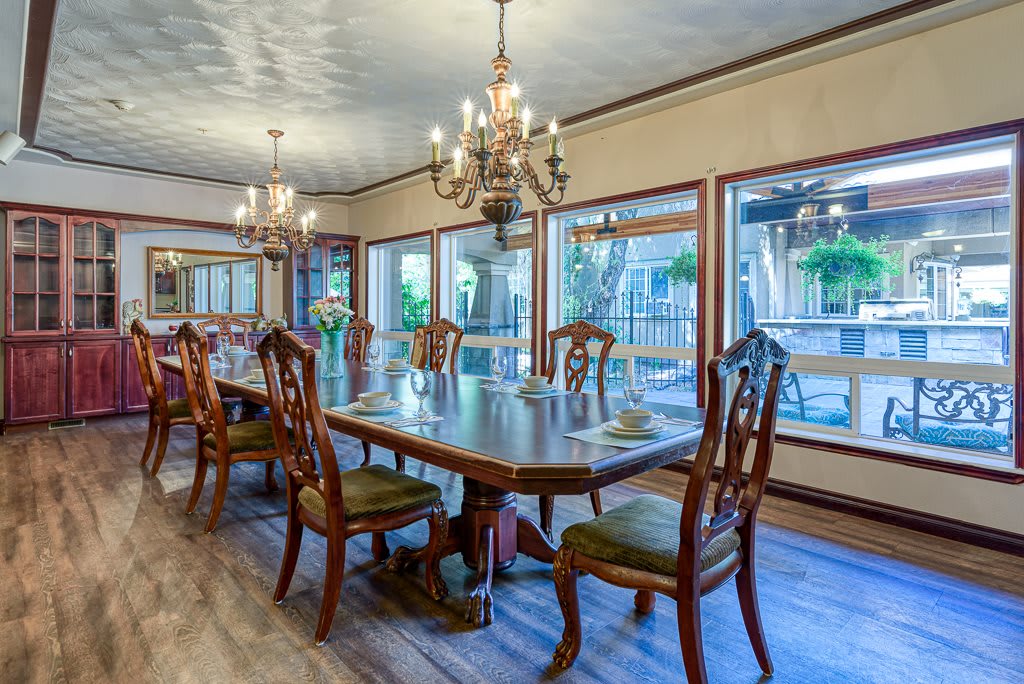 A spacious dining room with elegant chandeliers and wooden furniture, featuring large windows for natural light.
