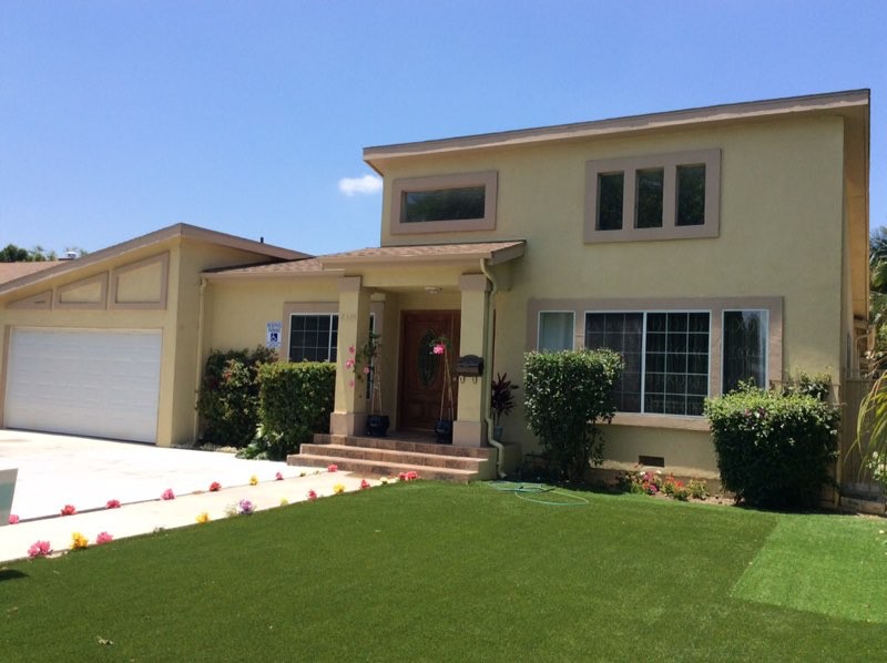 A suburban two-story house with a well-maintained lawn and large windows.