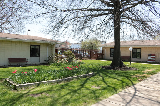 A tranquil view of a garden area with blooming flowers and a tree, surrounded by buildings under a clear sky.