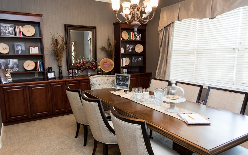 A neatly arranged dining room with a wooden table, upholstered chairs, and a chandelier.
