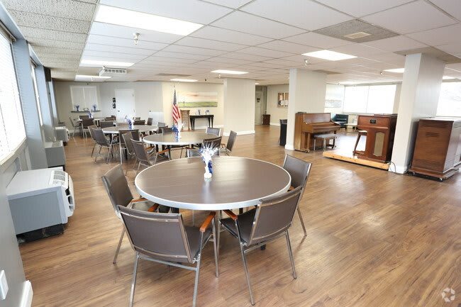 A spacious dining area with round tables and chairs, featuring a piano in the corner.