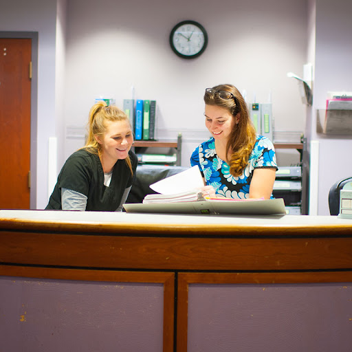 Two women engaged in a discussion at an office reception area.