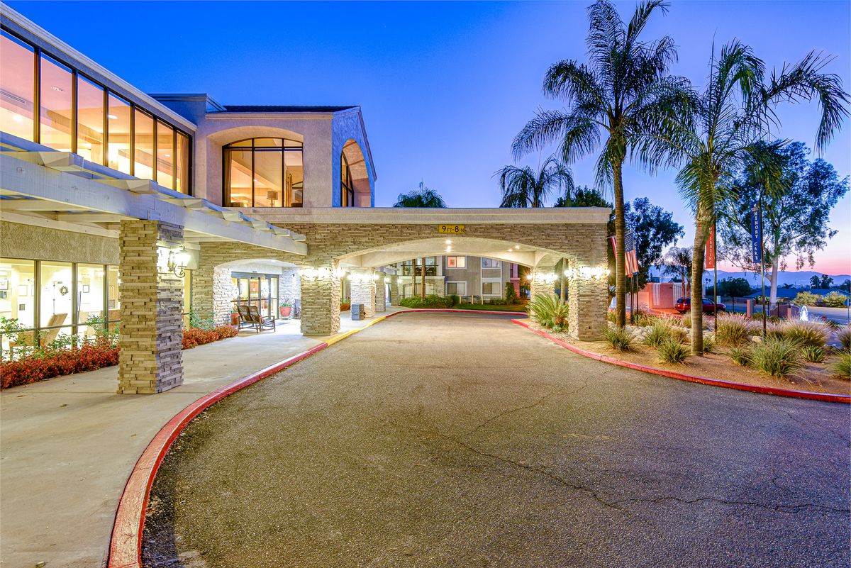 A well-lit hotel entrance with palm trees and modern architecture during the evening.