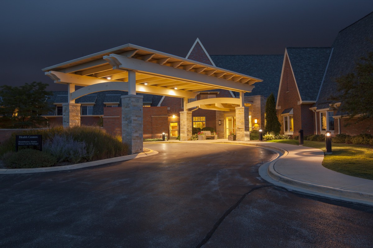 A well-lit building entrance at night with a covered driveway.