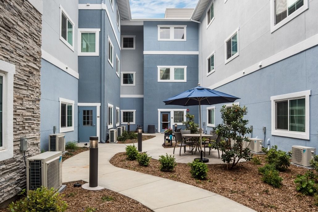 A modern apartment building featuring a courtyard with outdoor seating and a patio umbrella.