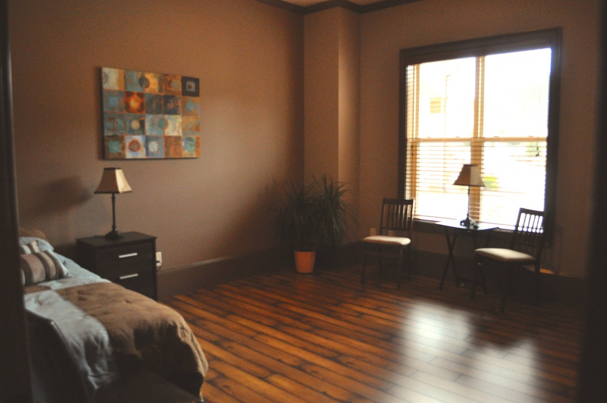 A cozy bedroom with hardwood flooring, modern decor, and natural light streaming through the window.