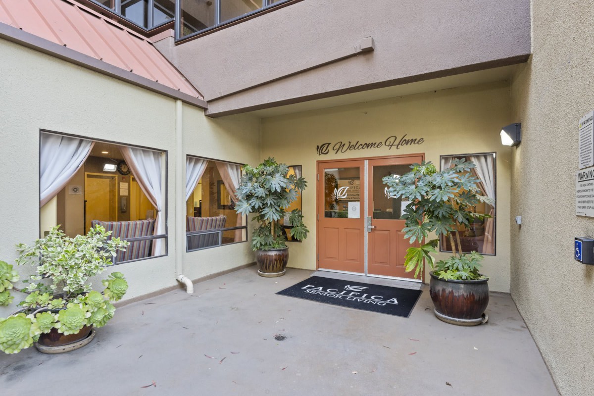 An inviting entrance to a building with large glass doors, adorned with potted plants and a welcome mat.