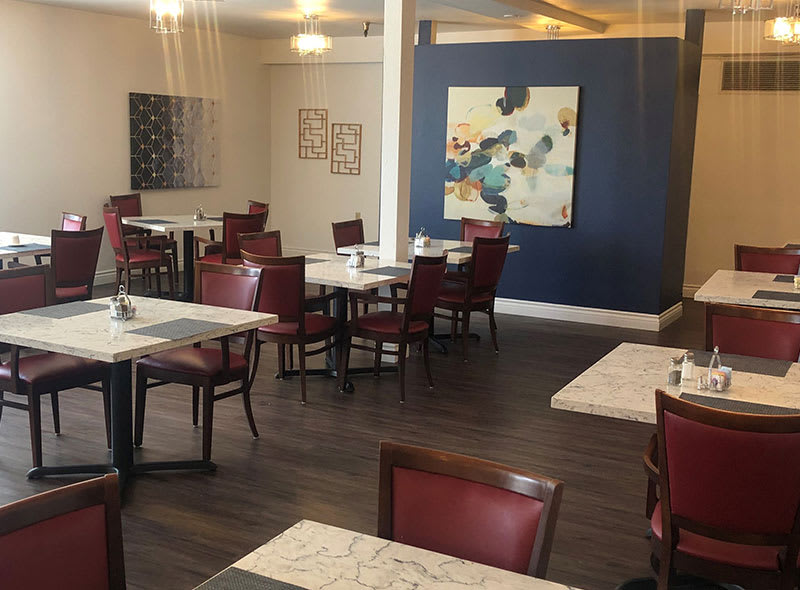 A modern restaurant interior with tables and chairs, adorned with artwork on the walls.