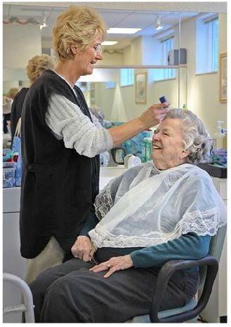An elderly woman enjoys a makeover at the hair salon, smiling as the hairdresser works on her.