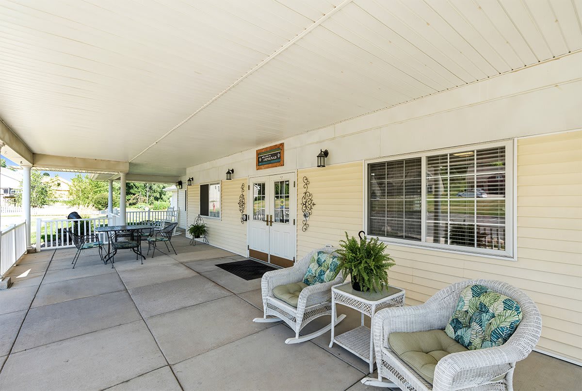 A covered patio with outdoor seating, featuring chairs, tables, and decorative plants.