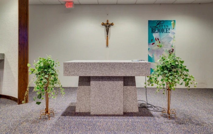An altar in a church featuring a cross on the wall, flanked by green plants.