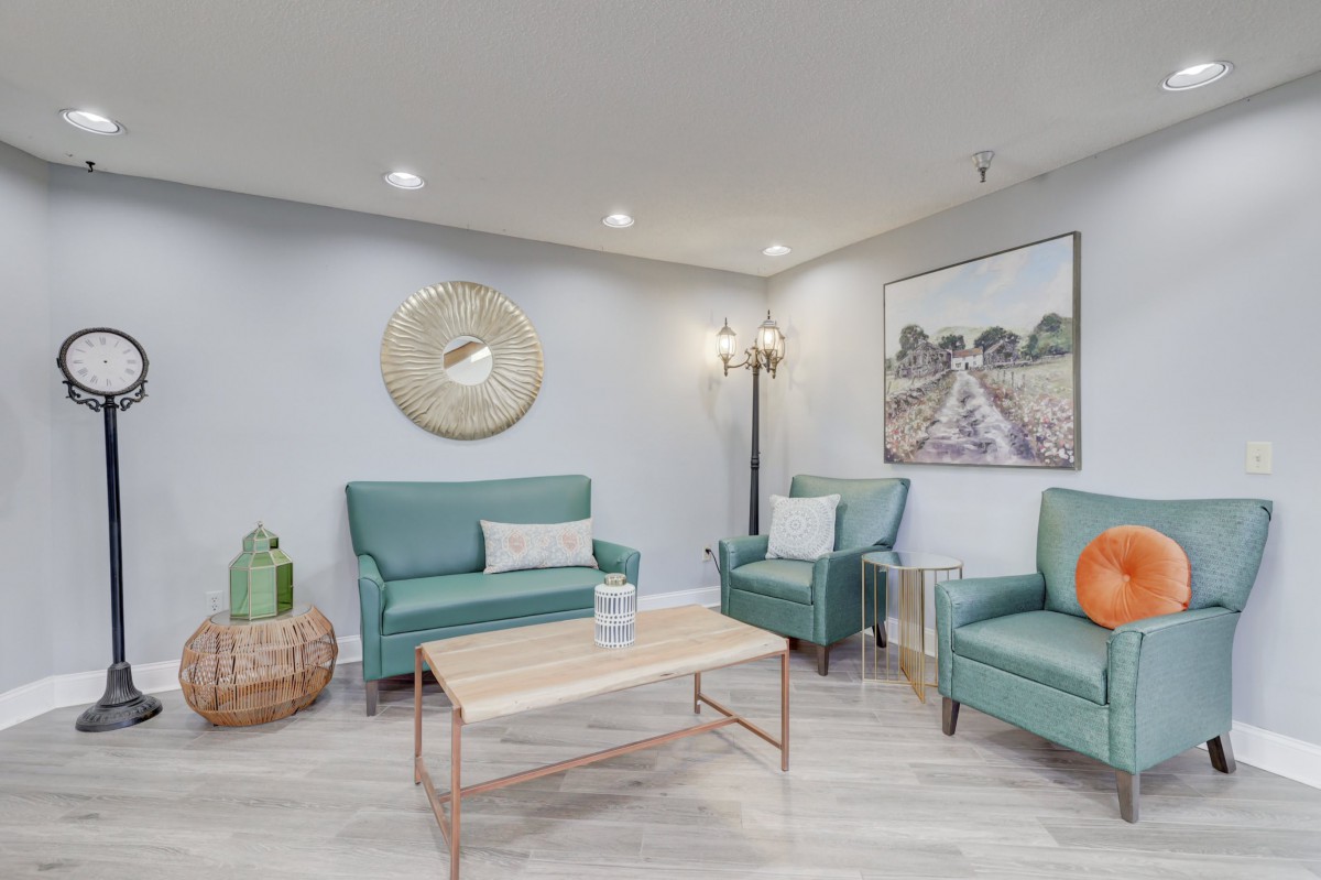A modern living room featuring teal sofas and armchairs, a wooden coffee table, and decorative artwork.