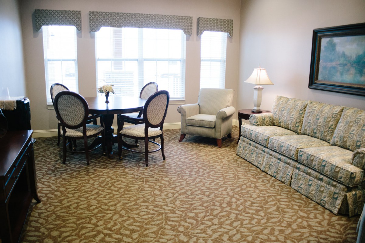 A cozy living room with a sofa, armchair, and a dining table near large windows.
