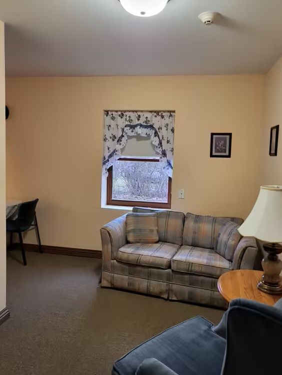 A cozy living room with a plaid sofa, lamp, and window with floral curtains.