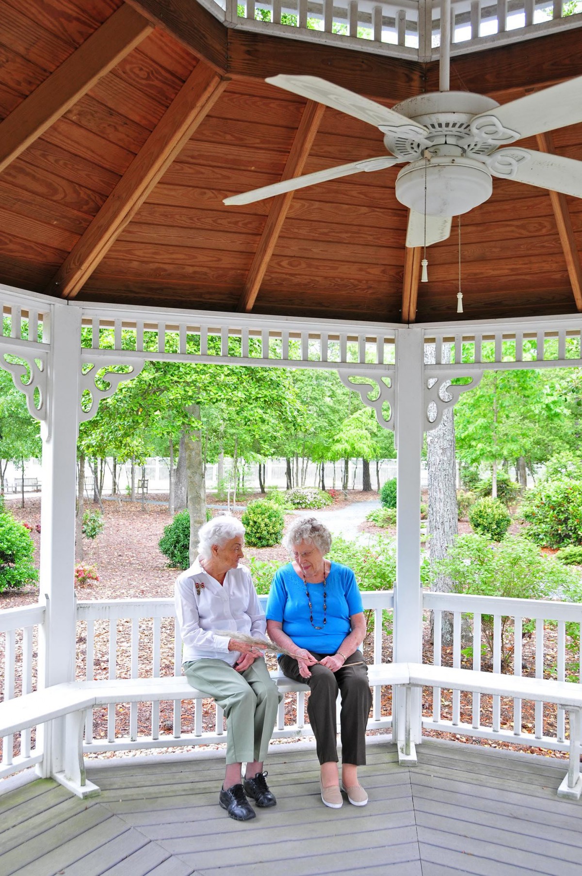 Two elderly individuals enjoying a conversation in a gazebo surrounded by lush greenery.