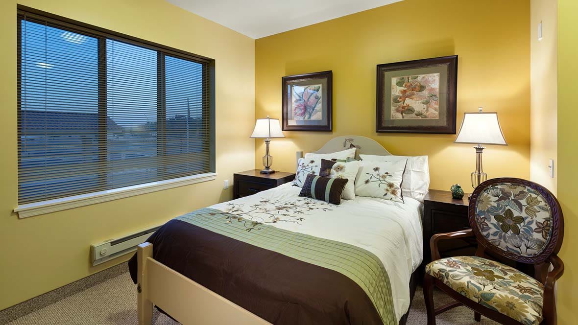 A cozy bedroom with a neatly made bed, decorative pillows, and framed artwork on the walls.