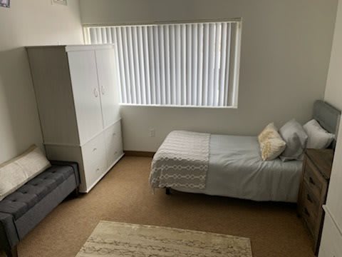 A minimalist bedroom with a single bed, wardrobe, and window blinds.