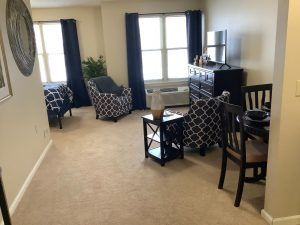 A cozy living room with patterned furniture, a carpeted floor, and large windows.