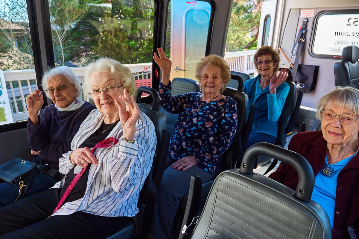 A group of elderly women smiling and waving on a bus ride.