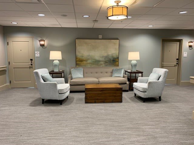 A cozy seating area with a sofa, two armchairs, and a coffee table, accented by lamps and artwork.