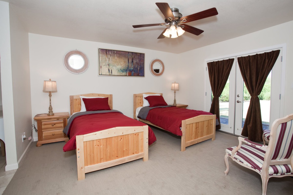 A cozy bedroom with twin beds, red bedding, and a ceiling fan.