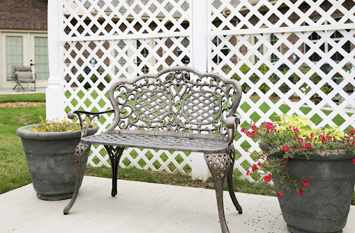 A decorative metal bench surrounded by flower pots against a lattice backdrop.