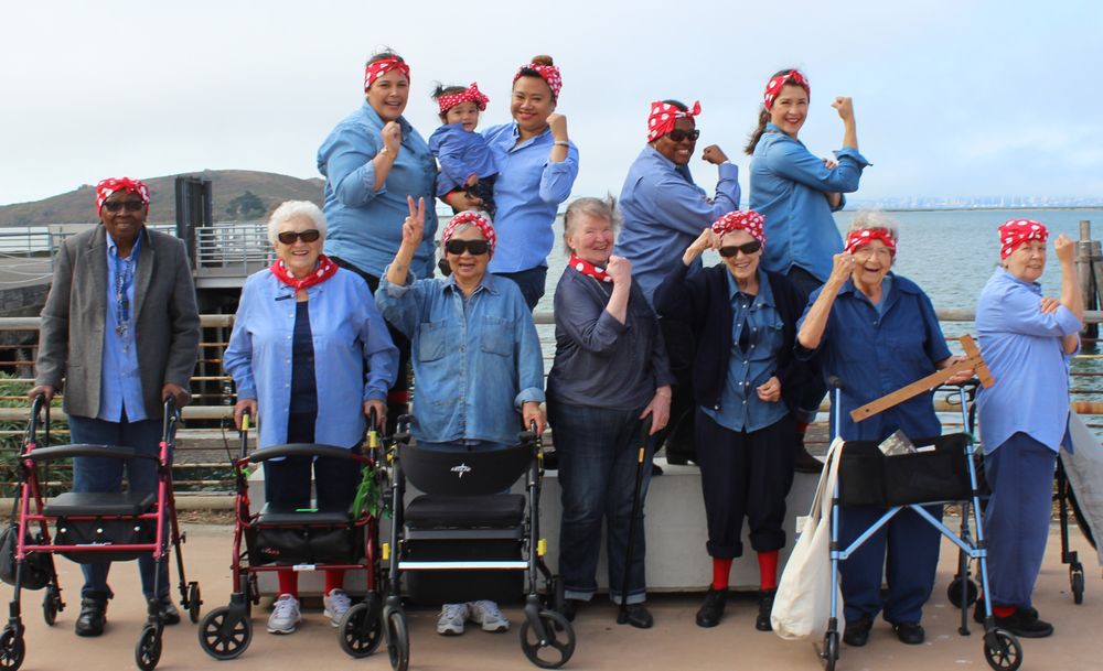 A group of women wearing matching costumes and bandanas pose and smile outdoors.